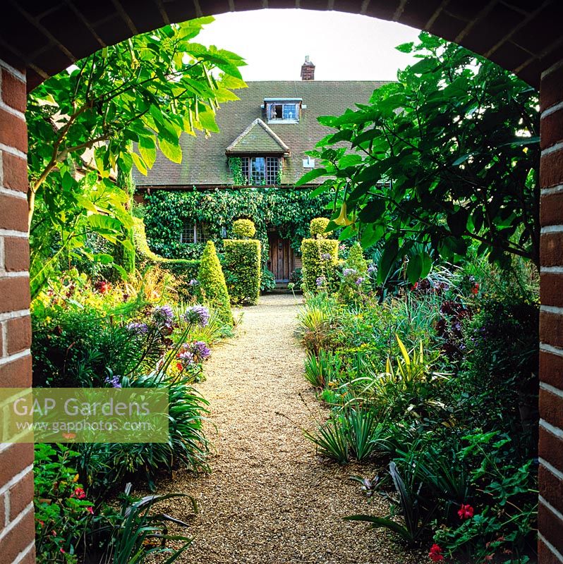 Walled Entrance to 1913 Arts and Crafts house, seen through brick arch past agapanthus and box topiary hedges.