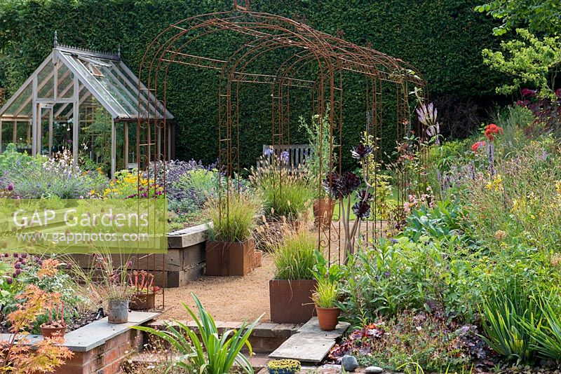 Rusty iron pergola divides garden of raised beds and border of late summer flowering perennials.