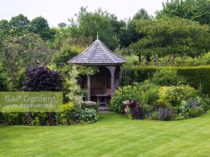 Summerhouse overlooking lawn, between borders of purple beech, euphorbia, dogwood, feverfew, hydrangea, snapdragon and orach.