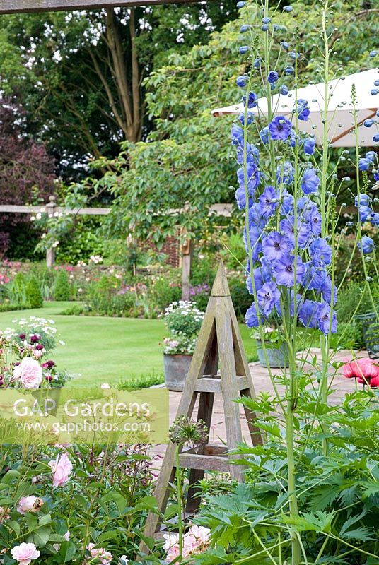 Obelisk in border with blue Delphinium and Rosa 'Felicia' - Priory House, Wiltshire