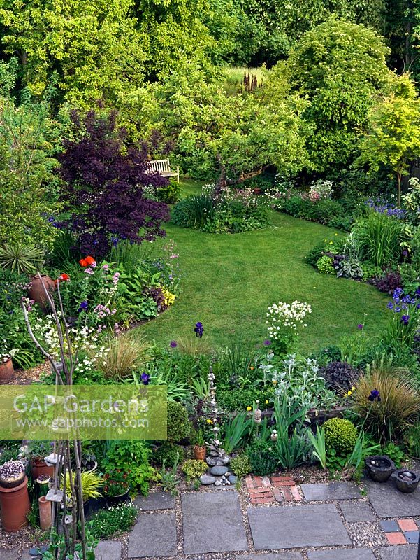 An old apple tree in the centre of a lawn shaped by deep curvaceous borders. Patio landscaped with blend of leftover materials. Viewed from upstairs bedroom window.