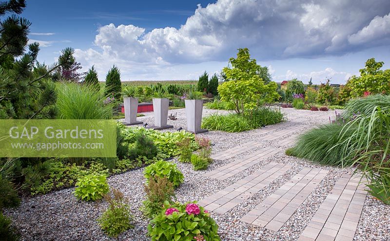 Modern garden with gravel and brick path. Tall containers planted with Yucca filomentosa
