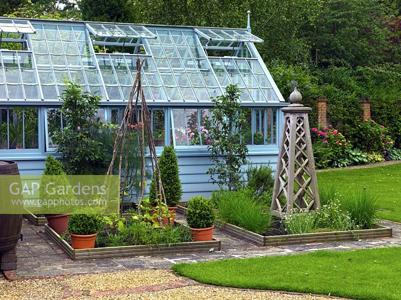 A vegetable garden with small raised beds in front of a painted wooden framed greenhouse.