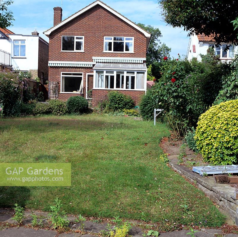 Before shot of rear of 1960s riverside home wedged between its neighbours. Dull red brick, ill proportioned windows and low-pitched gable need updating.