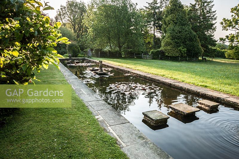 Formal lily pond with stepping stones serves as a ha ha dividing the garden from surrounding fields. King John's Nursery, Etchingham, East Sussex, UK