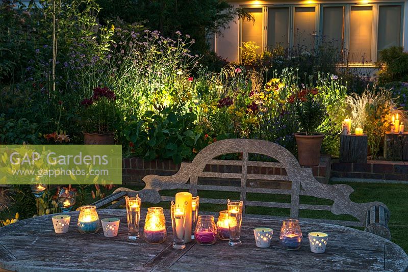 A table with candles and a backlit border illuminate a garden at night.