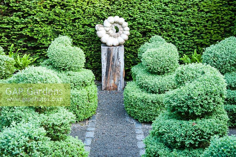 Ammonite sculpture by Darren Yeadon surrounded by box topiary, set within yew hedges. 