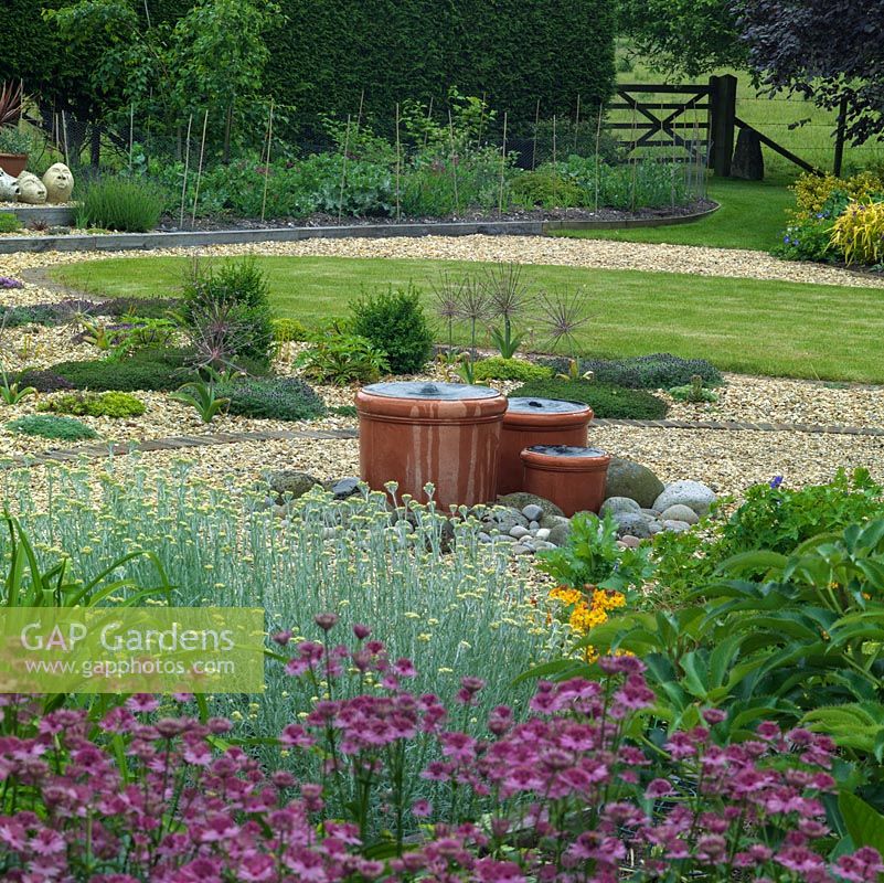 A water feature provides a focal point in a gravel garden. Planting includes Astrantia 'Roma',  santolina and Allium schubertii.