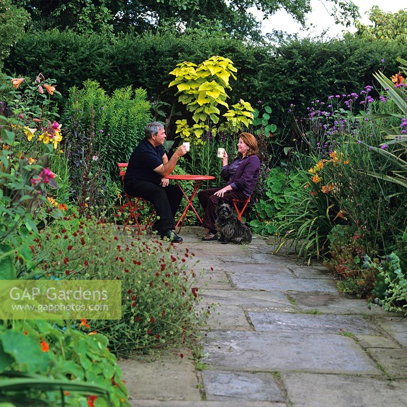 Chris and Sheila Bissell take a break in the hot garden with Digby, a Cairn terrier. Beds: Verbena bonariensis, nasturtium, Lilium African Queen, canna, daylily, catalpa.