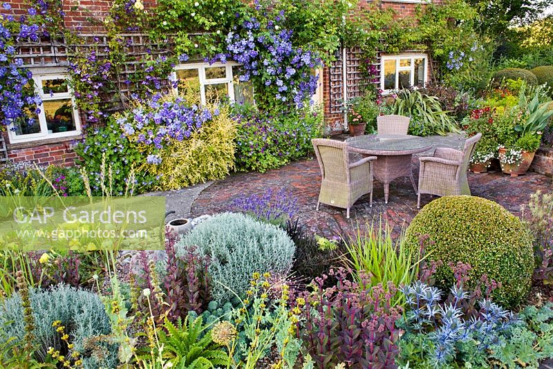 Planting includes: bed by house - Lonicera 'Baggesen's Gold', Clematis 'Perle d'Azur', Venosa Violacea, Geraniums 'Rozanne' and 'Ann Folkard'. In raised bed: Buxus, Santolina chamaecyparissus, Sedum 'Matrona', Eryngium 'Big Blue', Panicum 'Rotstrahlbusch', Ophiopogon plansicapus 'Nigrescens', Oenothera missouriensis, Morinia longifolia'
