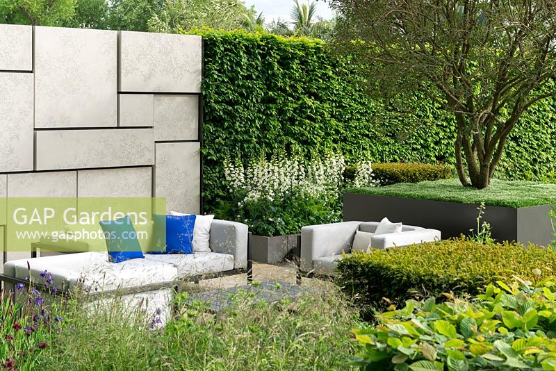 Within beds of perennials, grasses and yew blocks, a sunken seating area is backed by a wall and hornbeam hedge. The Telegraph Garden. RHS Chelsea Flower Show 2015