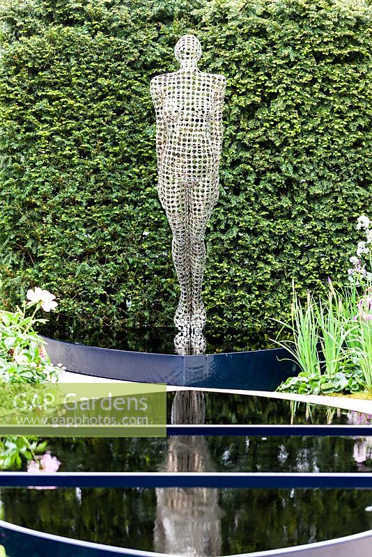 Stainless Steel sculpture in front of pool. Yew hedge behind. The Breakthrough Beast Cancer Garden. RHS Chelsea Flower Show, May 2015