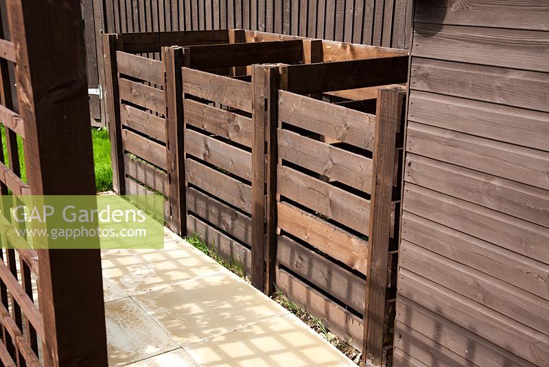 Three bay wooden compost bins located behind a timber trellis 