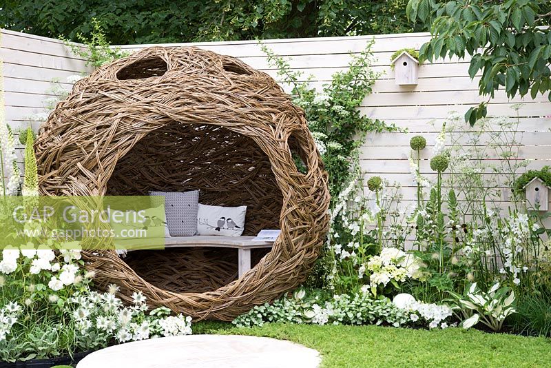 Spherical willow bird hide with bench, white flower borders with white painted fencing and bird houses - Living Landscapes: City Twitchers Garden, RHS Hampton Court Palace Flower Show 2015