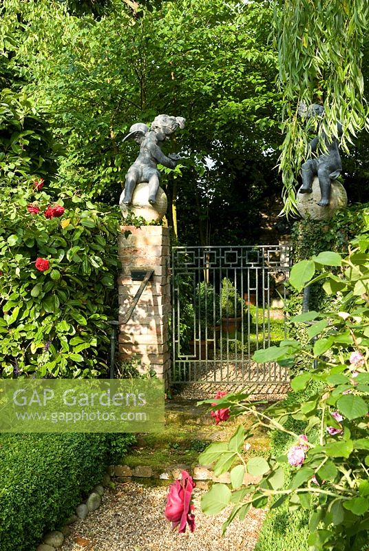 Two cherubs on stone spheres on the gate way which opens onto the Birch grove. The red rose - William Shakespeare, with Rosa Ferdinand Pichard. Paths edge with box hedging, a weeping willow partly hides one of the cherubs.