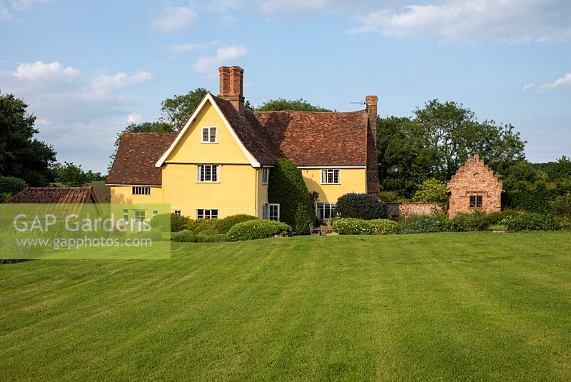 Old Suffolk house with sweeping lawn, shrubs and perennial borders, newly built brick garden house with a crow stepped gable. Heveningham, June