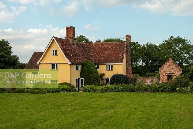 Old Suffolk house with sweeping lawn, Ceanothus, Laurus nobilis - bay tree by house with shrub and perennial borders. Newly built brick garden house with a crow stepped gable. Heveningham, June