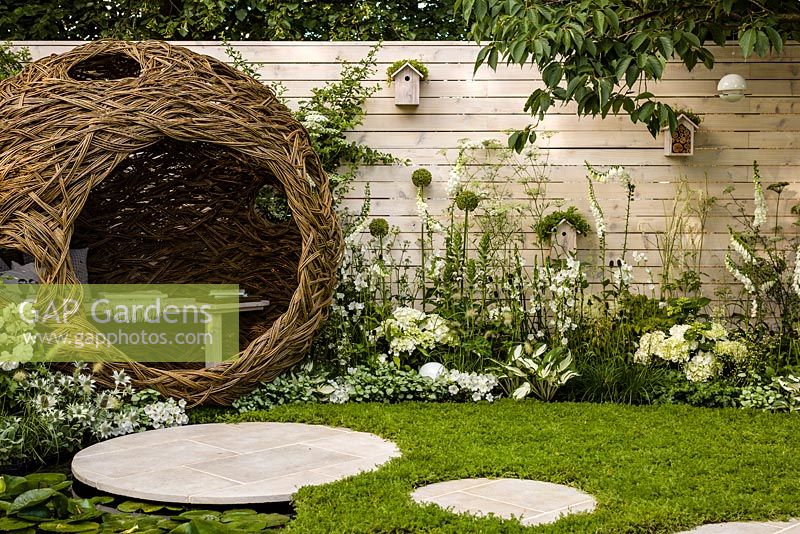 Living Landscapes 'City Twitchers' - view showing circular paved areas, camomile lawn, pond, spherical willow bird hide, nesting boxes and mixed planting in whites - RHS Hampton Court Flower Show 2015