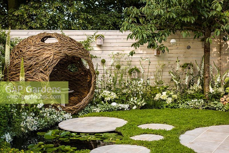 Living Landscapes 'City Twitchers' - view showing circular paved areas, camomile lawn, pond, spherical willow bird hide, nesting boxes, prunus tree and mixed white planting - RHS Hampton Court Flower Show 2015