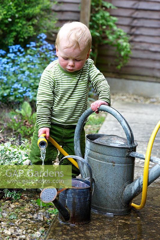 Little boy playing with watering cans and hose pipe