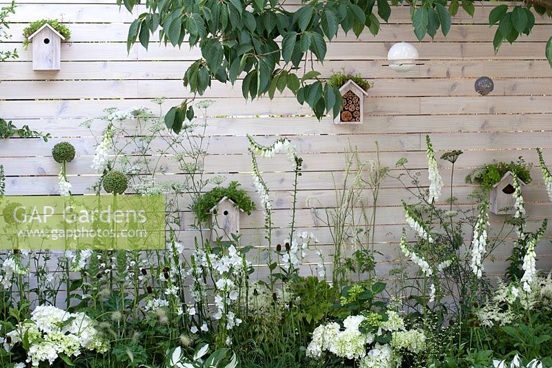 Birdboxes, insect hotels, bird feeders and white and green planting in Living Landscapes: City Twitchers garden at Hampton Court Palace Flower Show 2015