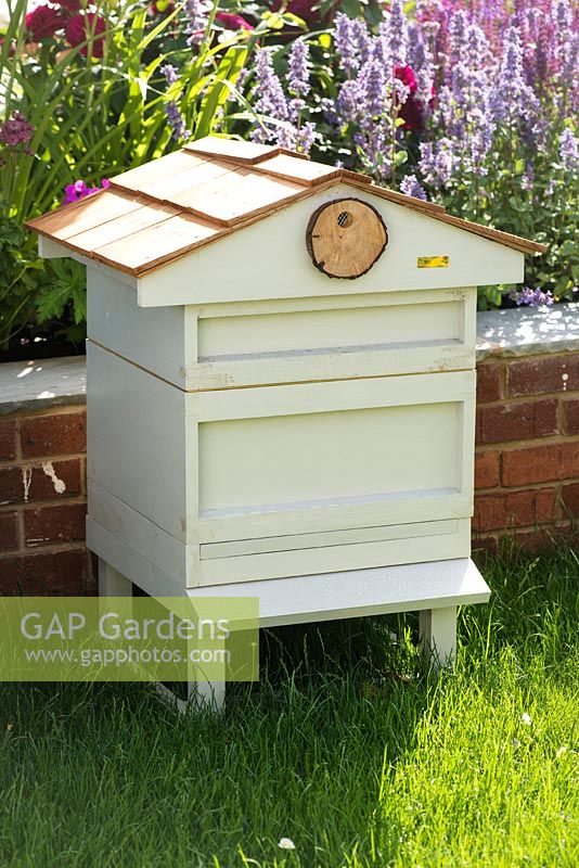 Just Retirement: A Garden For Every Retiree, white beehive placed in the garden against brick border with summer flowers. Designer: Tracy Foster Sponsor: Just Retirement Ltd