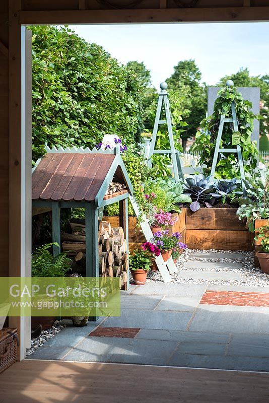 Just Retirement: A Garden For Every Retiree, view of rural garden with raised vegetable bed, plant support and wood store from a shed. Designer: Tracy Foster Sponsor: Just Retirement Ltd