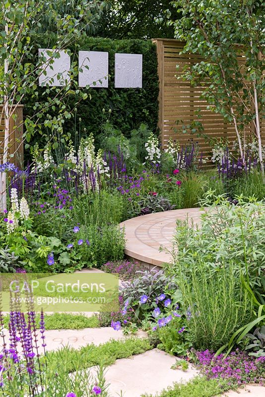The Wellbeing of Women Garden. a circular patio is edged in medicinal and sensory plants, in purples, blues and whites. Designers: Claire Moreno, Wendy von Buren and Amy Robertson.