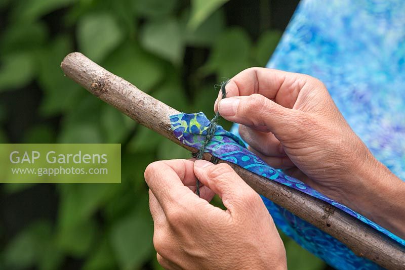 Securing fabric to hazel sticks using string, to create an awning canopy