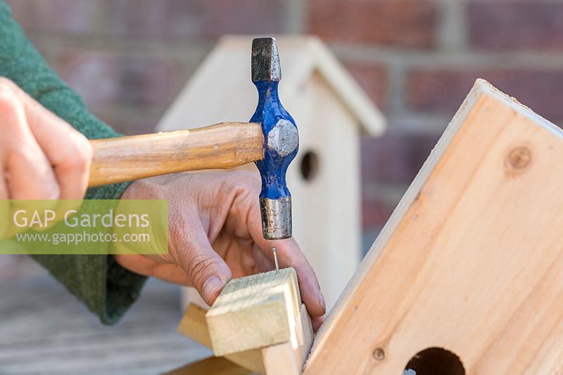 Secure the wooden batons to the roof of the bird house using a hammer