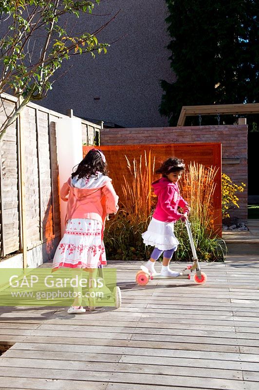 Small urban contemporary town garden children kids playing on decked patio terrace.  Ansari garden, Harrow