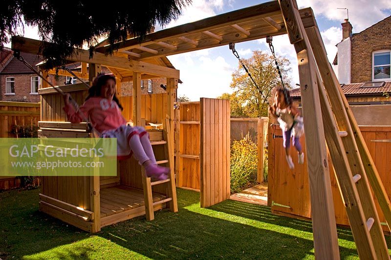 Girl on swing. Children's play area with wooden climbing frame. Small urban contemporary town garden. Ansari garden, Harrow