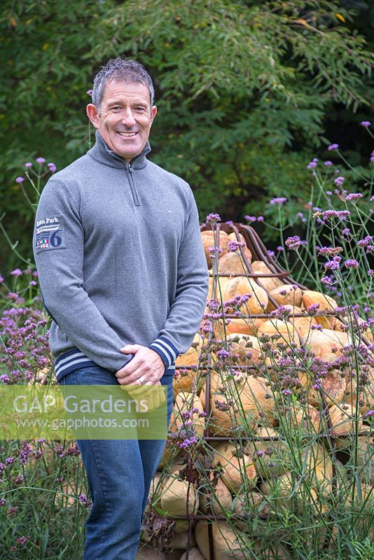 Garden designer Sean Butler of Cube 1994, standing beside a unique Gabion sculpture shaped like a bulb, with planting of Verbena bonariensis and Actaea