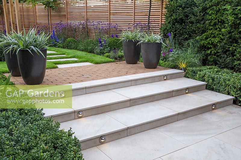 Marble steps with lighting feature at dusk. Verbena bonariensis and Calamagrostis x acutiflora 'Karl Foerster' in foreground and potted Astelia chathamica