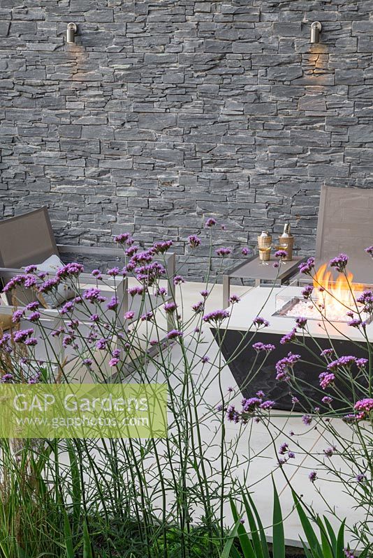 View through the border of Verbena bonariensis and Calamagrostis x acutiflora 'Karl Foerster' to the sunken seating area with liquid propane fire pit and dry stone slate wall