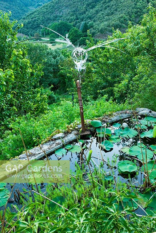 Lily pond with 'half bird, half insect - Guardian Des Sambucs' sculpture by Manu Rodriguez. 