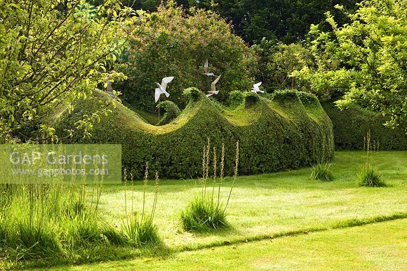 Seagull sculptures of stainless steel fly over topiary Buxus - Box hedges clipped into wave crests. Farleigh House, Hampshire. Designer Georgia Langton. Seagulls by Diane Maclean