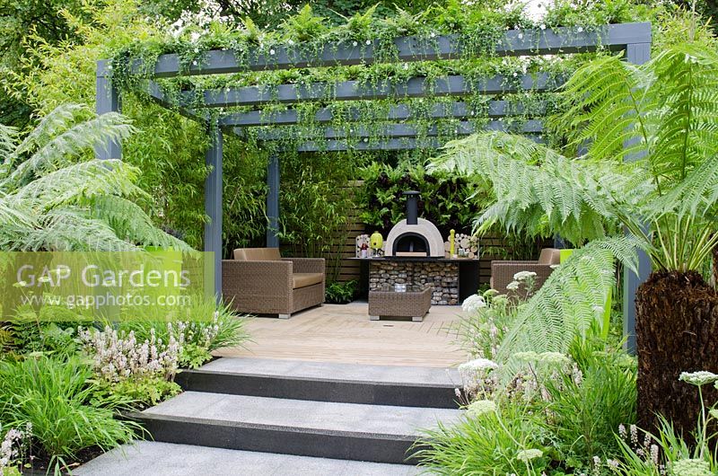 Steps leading up to pergola with Vinca minor 'Alba' and Polystichum polyblepharum, outdoor wood fired oven on table made from wire cage filled with pebbles, borders include Dicksonia antarctica, Cenolophium denudatum and Tiarella  - Live Outdoors, RHS Hampton Court Palace Flower Show 2012