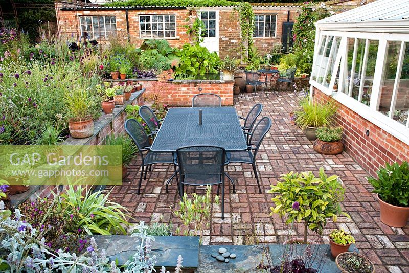 Sunken patio beside the conservatory enclosed with brick wall and perennial borders. The Coach House