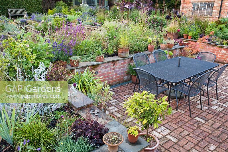Sunken patio beside the conservatory enclosed with brick wall and perennial borders. The Coach House