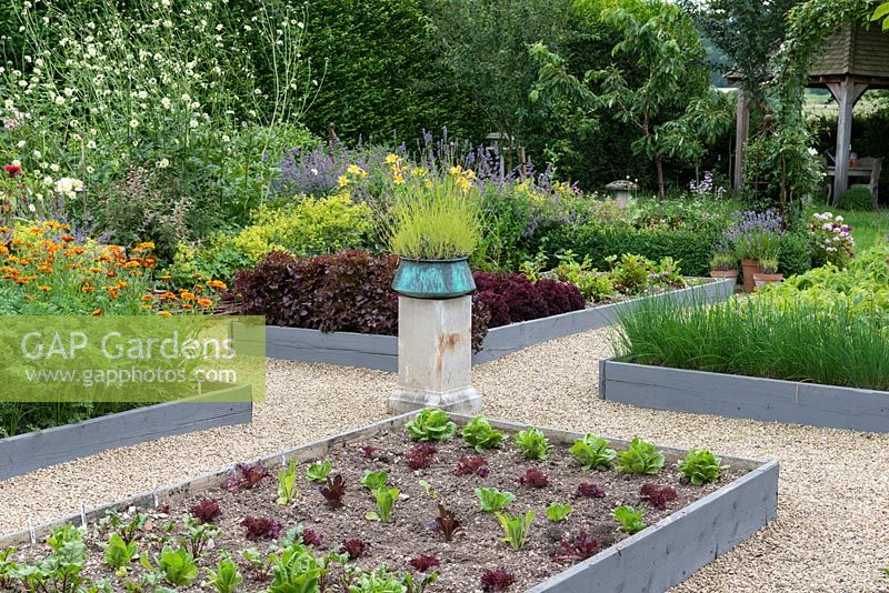 A potager with raised beds of chives and salad. A stone plith with a copper pot of  lavender provides a focal point on the central axis.