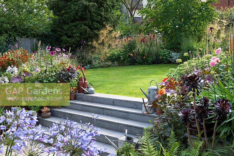 Stone steps leading to a lawn surrounded by colourful late summer borders and containers with perennials and succulents.