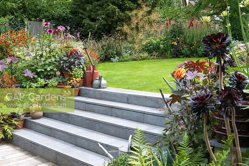 Stone steps leading to a lawn surrounded by colourful late summer borders and containers with perennials and succulents.