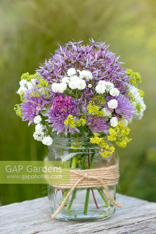 A summer posie with alliums, gypsophila and alchemilla in a glass gar decorated with twine.