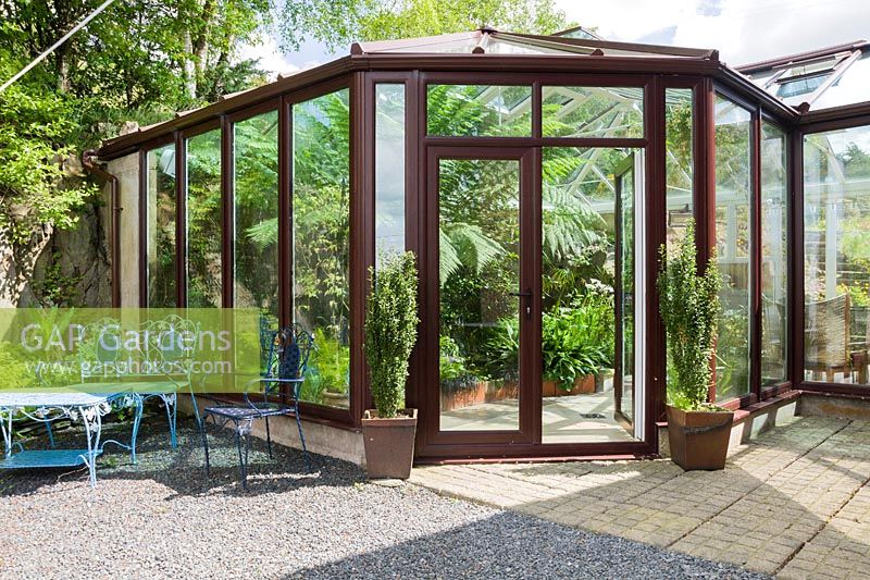Conservatory that links the back of the house with a rocky outcrop behind it, with pond and border inside containing plants that would struggle to survive outside such as a tree fern, Dicksonia antarctica, Geraniums palmatum and aspidistras. Windy Hall, Windermere, Cumbria, UK