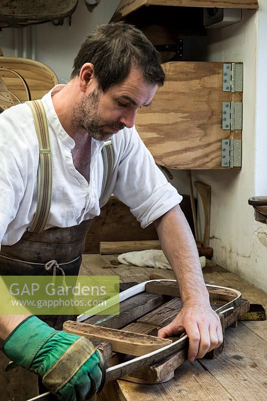 Charlie Groves making a traditional Sussex trug. After being steam bent, a length of sweet chesnut is bent round the former, a frame to create the rim of the trug.
