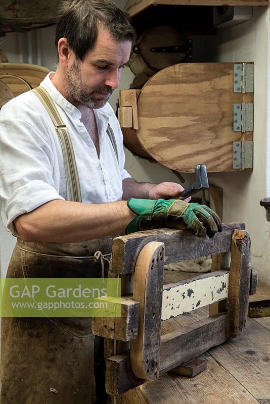 Charlie Groves making a traditional Sussex trug. Pinning the trug's rim together with a nail. Behind, the Heath Robinson style steamer.