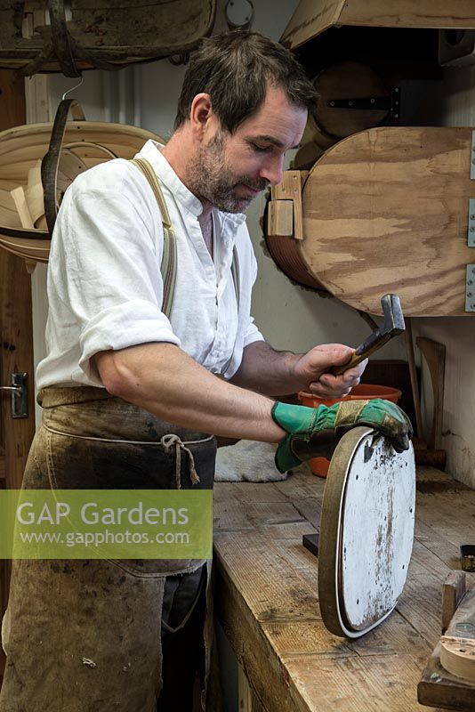 Charlie Groves making a traditional Sussex trug. After being steam bent, a length of sweet chesnut is bent round the former, a frame to create the trug handle. Behind, the Heath Robinson style steamer.