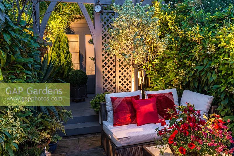 A small contemporary garden with outdoor living area lit at night.