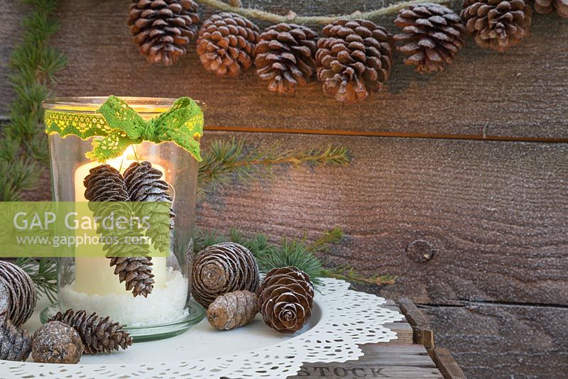 A candle jar decorated with a green laced bow and pine cones